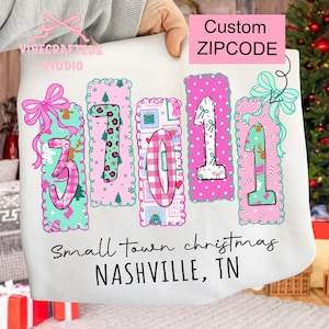 May include: A white sweatshirt with the text "Small town christmas NASHVILLE, TN." The design features the numbers "37101" in pink, teal, and green, with decorative bows and patterns. The words "Custom ZIPCODE" are also visible on the sweatshirt.