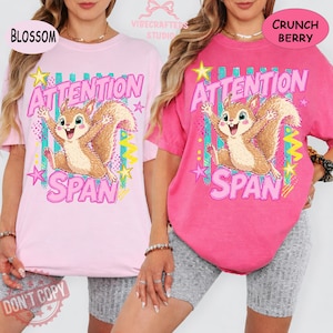 Może przedstawiać: Dwie koszulki, jedna jasnoróżowa i jedna intensywnie różowa, z nadrukiem wiewiórki z kreskówki i napisem "ATTENTION SPAN". Wiewiórka jest brązowa i brązowa z wesołą miną. Koszulki mają luźny krój.