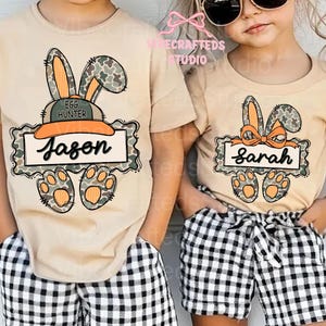 May include: Two tan t-shirts with Easter bunny designs. One shirt has "Jason" on a banner, the other has "Sarah". Both shirts feature bunny ears, paw prints, and a camouflage pattern. The children are wearing black and white checkered shorts.