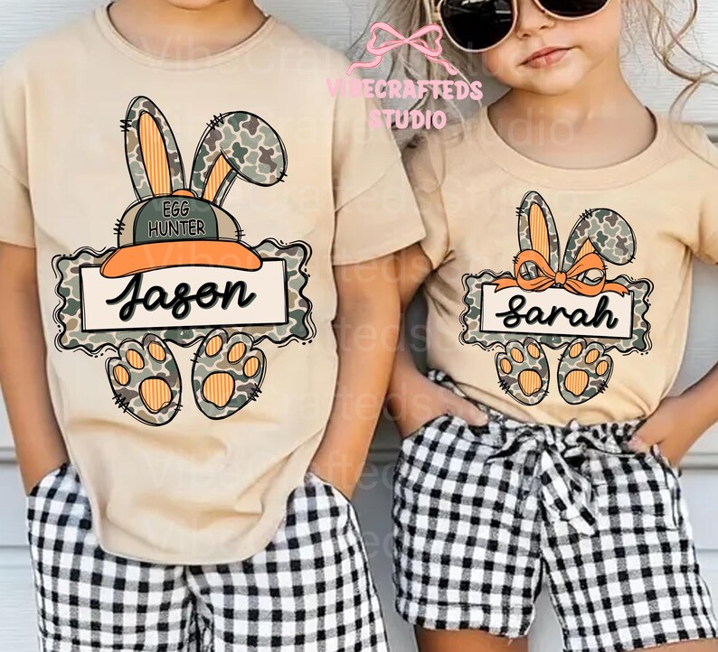 May include: Two tan t-shirts with Easter bunny designs. One shirt has "Jason" on a banner, the other has "Sarah". Both shirts feature bunny ears, paw prints, and a camouflage pattern. The children are wearing black and white checkered shorts.