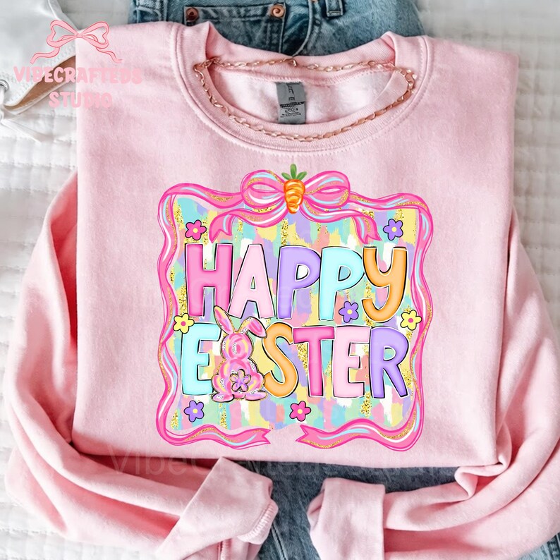 May include: A light pink sweatshirt with a colorful "Happy Easter" graphic. The graphic features a bunny, flowers, and a bow. The text is in pastel colors, with a carrot on top. A gold chain is around the neck.