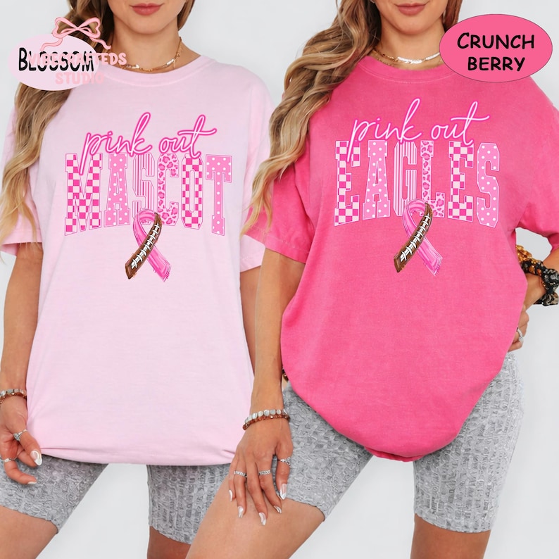 May include: Two short-sleeve t-shirts in light pink and dark pink. The light pink shirt features the text "pink out MASCOT" and the dark pink shirt features "pink out EAGLES" with a brown football-patterned ribbon graphic on each shirt.