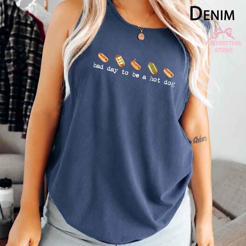May include: A dark blue sleeveless tank top featuring a graphic of five small hot dogs arranged in a row above the white text that reads, bad day to be a hot dog. The shirt has a round neckline and a relaxed fit, showcasing a casual style.