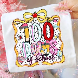 Puede incluir: Camiseta blanca con un gr&aacute;fico colorido que celebra los 100 d&iacute;as de escuela. El dise&ntilde;o incluye un gran "100" con un l&aacute;piz y una manzana, adem&aacute;s de las palabras "Days of School". Una cinta amarilla y detalles florales enmarcan el dise&ntilde;o.