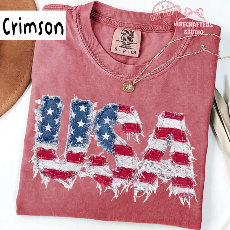 Pu&ograve; includere: T-shirt color cremisi con la scritta "USA" in un design a bandiera americana invecchiata. Le lettere presentano denim blu con stelle bianche e tessuto a righe rosse e bianche. Una collana d'argento con un ciondolo &egrave; sulla maglietta.
