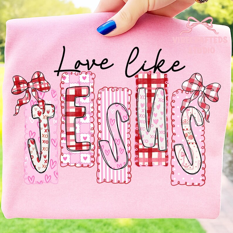 May include: Pink t-shirt with the words "Love like Jesus" in black script. The word "Jesus" is spelled out in decorative letters with hearts, gingham, and stripes. Red and white gingham bows adorn the top of the letters.