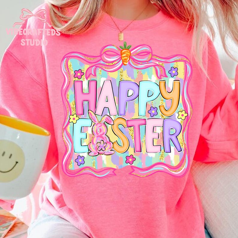 May include: Pink sweatshirt with a colorful "Happy Easter" graphic. The design includes a bunny, flowers, and a bow with a carrot. The text is in pastel colors, perfect for Easter celebrations.