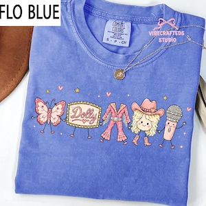 May include: A periwinkle blue t-shirt featuring a graphic print of a butterfly, a marquee sign with the text Dolly, a pink fringe outfit, a blonde character wearing a cowboy hat and boots, and a microphone, all holding hands with small stars.