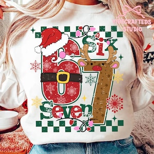 May include: White sweatshirt with a festive Christmas design. The graphic features the number "67" with a Santa Claus hat, reindeer antlers, and the word "Seven". The design includes snowflakes, string lights, and a green and white checkered border.
