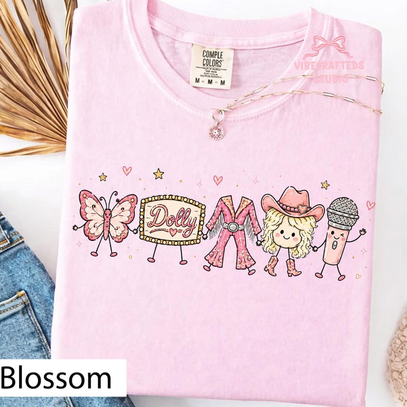 May include: A light pink t-shirt featuring a graphic print of a butterfly, a marquee sign with the text Dolly, a pink fringe outfit, a blonde character wearing a cowboy hat and boots, and a microphone, all holding hands with small hearts and stars.