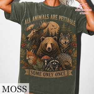 Pu&ograve; includere: Una t-shirt a maniche corte color verde muschio con una stampa grafica raffigurante un alce, un orso, un lupo, una volpe, un procione e un riccio in un bosco. Il testo recita ALL ANIMALS ARE PETTABLE e SOME ONLY ONCE.