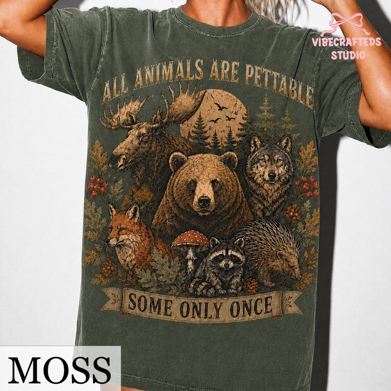 Pu&ograve; includere: Una t-shirt a maniche corte color verde muschio con una stampa grafica raffigurante un alce, un orso, un lupo, una volpe, un procione e un riccio in un bosco. Il testo recita ALL ANIMALS ARE PETTABLE e SOME ONLY ONCE.