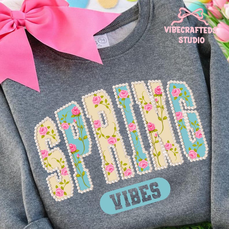 May include: A gray sweatshirt with the word "SPRING" in a floral design, with pink roses and a light blue background. The word "VIBES" is below the word "SPRING". A large pink bow is in the upper left corner.
