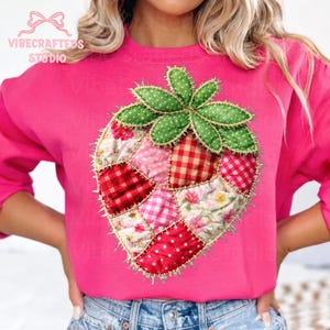 Puede incluir: Una sudadera rosa brillante con un diseño de fresa de patchwork. La fresa está compuesta por varios patrones de tela, incluyendo cuadros, lunares y estampados florales, con hojas verdes. El texto "VIBECRAFTEDS STUDIO" es visible.