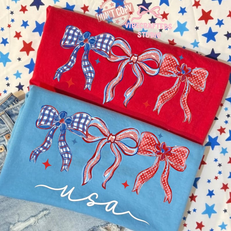 May include: Red and blue t-shirts with bow designs. One shirt is red, the other is blue, and both feature a bow design with red, white, and blue accents. The blue shirt has the word "usa" in white script.