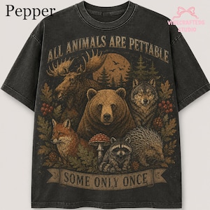 Pu&ograve; includere: Una t-shirt grigio antracite a maniche corte con una stampa grafica raffigurante un alce, un orso, un lupo, una volpe, un procione e un istrice in una foresta. Il testo recita ALL ANIMALS ARE PETTABLE sopra e SOME ONLY ONCE sotto.