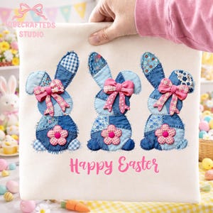 May include: A cream-colored Easter-themed fabric panel featuring three patchwork bunny figures in denim and floral fabrics. Each bunny has a pink bow and a flower. The words "Happy Easter" are printed in pink.