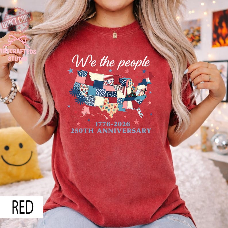 May include: A red t-shirt with a patchwork map of the United States. The words "We the people" are above the map, with "1776-2026 250TH ANNIVERSARY" below. The shirt is a casual style.