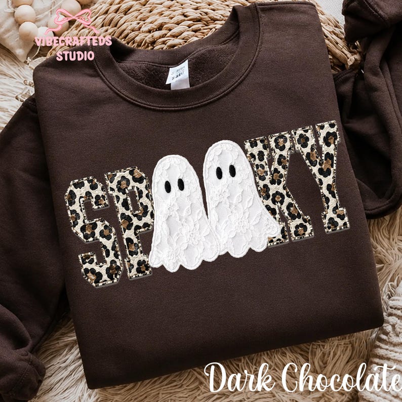 May include: A dark chocolate brown crewneck sweatshirt featuring the word SPOOKY in a leopard print pattern. The two letter O's are replaced by white lace ghost figures with black eyes. The sweatshirt has a ribbed collar and long sleeves.