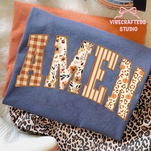 Puede incluir: Una sudadera azul con la palabra "AMEN" en una fuente decorativa. Las letras están rellenas de patrones de cuadros, florales, rayas y leopardo. La sudadera está superpuesta a una camiseta naranja y a una tela con estampado de leopardo.