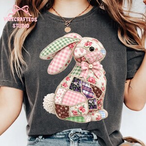 May include: Dark gray t-shirt featuring a patchwork bunny design. The bunny has pink, green, and purple patterned patches, a pink bow, and a fluffy white tail. The text "VIBECRAFTED STUDIO" is printed at the top left.