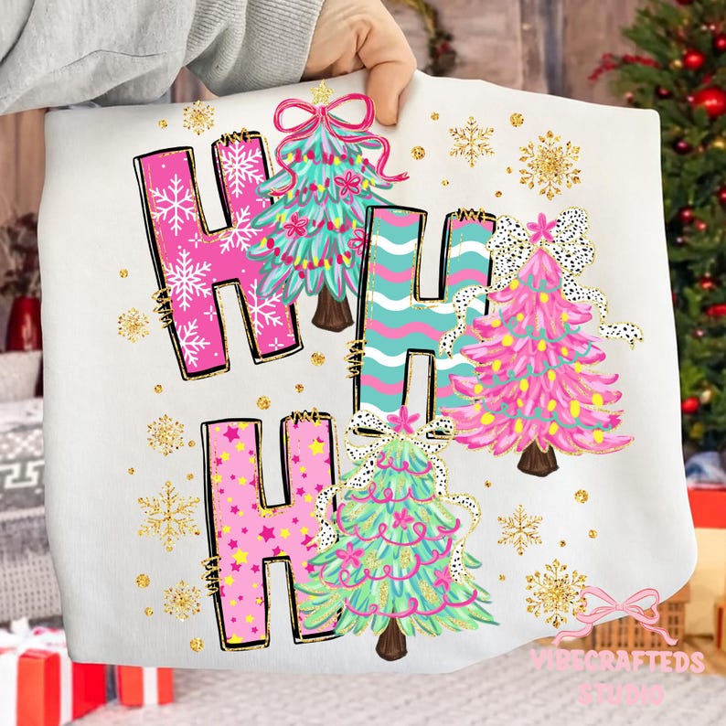 May include: White sweatshirt with the words "HO HO HO" in pink and teal letters, decorated with Christmas trees and snowflakes. The letters are outlined in gold, and the trees have bows.