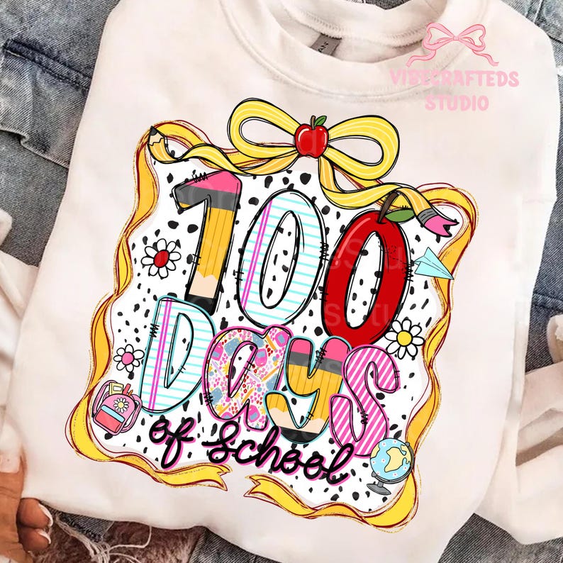 Puede incluir: Sudadera blanca con un gr&aacute;fico colorido que celebra los 100 d&iacute;as de escuela. El dise&ntilde;o incluye el texto "100 Days of School" con l&aacute;pices, una manzana, flores y un globo terr&aacute;queo. Una cinta y un lazo amarillos enmarcan el dise&ntilde;o.