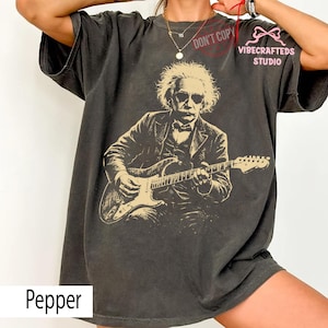 May include: Pepper-colored t-shirt featuring a sepia-toned image of Albert Einstein playing an electric guitar. The graphic includes Einstein wearing sunglasses and a suit. The shirt has the text "DON'T COPY" and "VIBECRAFTED STUDIO".