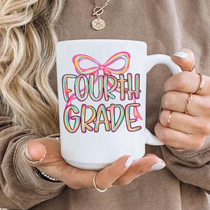 Pode incluir: Caneca de cer&acirc;mica branca com as palavras "FOURTH GRADE" em letras coloridas e um desenho de la&ccedil;o. A caneca tem uma al&ccedil;a branca.