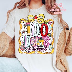 Puede incluir: Camiseta blanca con un gr&aacute;fico colorido que celebra "100 d&iacute;as de escuela". El dise&ntilde;o presenta un gran "100" con un l&aacute;piz, una manzana y otros elementos tem&aacute;ticos escolares. El texto "Days of School" est&aacute; escrito debajo de los n&uacute;meros.