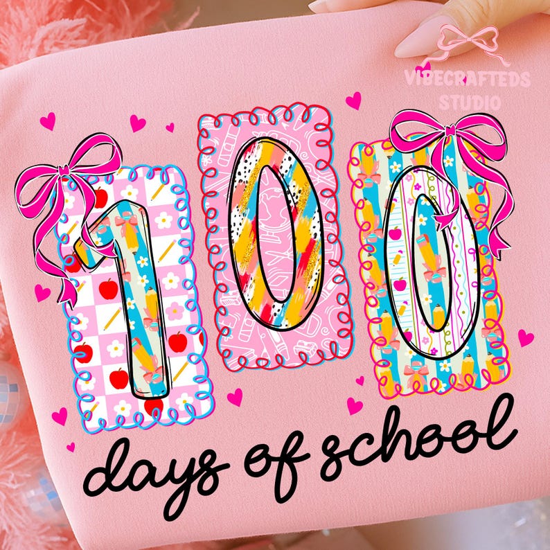 May include: Pink graphic tee with the text "100 days of school." The design features the numbers "100" in colorful patterns, decorated with bows and hearts. The tee is from VibeCrafteds Studio.