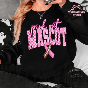 May include: A black long-sleeve sweatshirt featuring the pink text "pink out" above the word "MASCOT" in a large, blocky font with various pink patterns including checkers, polka dots, and leopard print, plus a pink awareness ribbon football graphic.