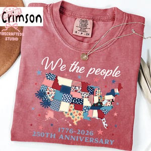 May include: Crimson red t-shirt with the text "We the people" and a patchwork map of the United States. The shirt also features the text "1776-2026 250th Anniversary". A silver necklace with a pendant is on the shirt.