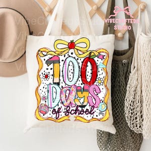Puede incluir: Un bolso tote blanco con un gr&aacute;fico colorido que celebra "100 d&iacute;as de escuela". El dise&ntilde;o incluye un gran "100" con una manzana roja, l&aacute;pices y las palabras "Days of School" en una fuente l&uacute;dica. La bolsa tiene una cinta amarilla y lunares negros.
