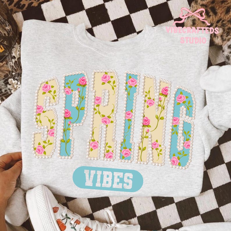May include: Light gray sweatshirt with the word "SPRING" in large, decorative letters. The letters are cream-colored with blue accents and adorned with pink roses and pearls. Below, a light blue oval reads "VIBES".