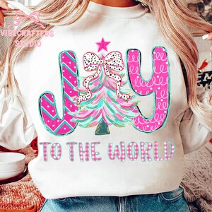 May include: White sweatshirt with a colorful Christmas tree design and the words "JOY TO THE WORLD." The tree is pink and teal with a polka dot bow and star. The letters are pink and teal.