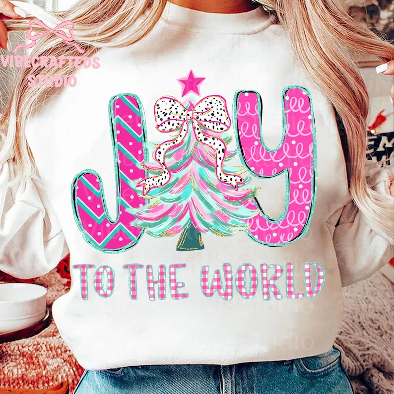 May include: White sweatshirt with a colorful Christmas tree design and the words "JOY TO THE WORLD." The tree is pink and teal with a polka dot bow and star. The letters are pink and teal.