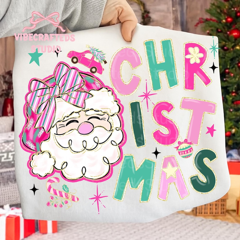 May include: White sweatshirt with a colorful Christmas design. The design features a Santa Claus with a pink and green hat and bow, a pink car with a Christmas tree, and the word "CHRISTMAS" in pink and green letters.
