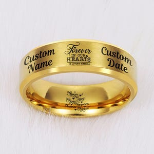 May include: A gold-colored ring with engraved text. The ring features the words "Custom Name" and "Custom Date" on either side of "Forever in our Hearts in Loving Memory." Inside the ring are the words "Always Loved, Never Forgotten, Forever Missed."