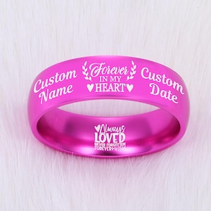 May include: A bright pink ring with white engraved text. The ring features the words "Custom Name" and "Custom Date" on either side of "Forever in my Heart." The inside of the ring reads "Always Loved, Never Forgotten, Forever Missed."
