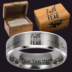 May include: A silver ring with the words "Faith Over Fear" and "Your Text Here" engraved on it. The ring is displayed with two wooden boxes, one open and lined with fabric, and the other closed with the same phrase on the lid.