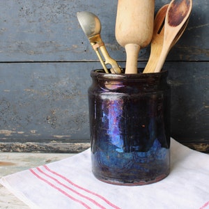 May include: A blue and black ceramic utensil holder with a wooden spoon, a wooden ladle, and a brass ice cream scoop inside.