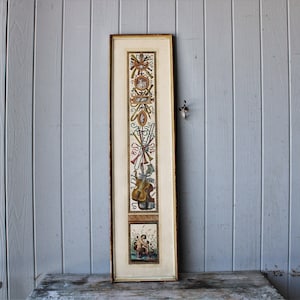 Puede incluir: Una obra de arte enmarcada, vertical, con una ilustración detallada de instrumentos musicales y figuras clásicas. La obra incluye un violín, trompas y otros instrumentos, con un marco dorado. El fondo es de color crema claro, sobre una superficie de madera envejecida.