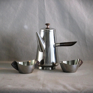 May include: A polished stainless steel coffee pot with a dark brown wooden handle and lid knob, accompanied by two matching small stainless steel bowls featuring dark brown wooden side accents, all arranged together on a neutral surface.