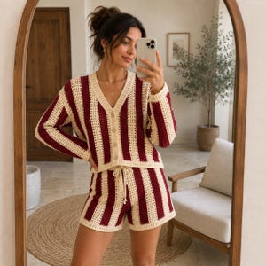 May include: A two-piece crochet set featuring a long-sleeve button-down cardigan and matching shorts. The garment is designed with vertical stripes in deep burgundy and cream colours. The cardigan has a V-neckline and the shorts have a drawstring waist.