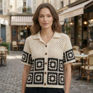 May include: A short-sleeved button-down shirt featuring a crochet granny square pattern. The top portion is cream-colored, while the lower section and sleeves are composed of black and cream-colored floral-style crochet squares with a collar.