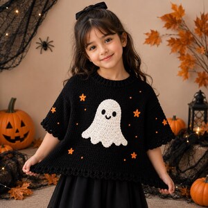 May include: A black crochet sweater featuring a white ghost motif in the center, accented with small orange stars and dots. The sweater has a round neckline, short sleeves with a scalloped edge, and a matching scalloped hemline design.