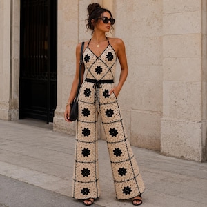 Può includere: Tuta all'uncinetto beige e nera con motivo floreale. La tuta ha una vita con coulisse e gambe larghe. L'outfit è completato da sandali neri e una borsa nera.