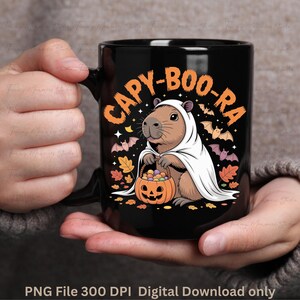 May include: Black ceramic mug featuring a Halloween-themed design. The mug displays a capybara dressed as a ghost, holding a pumpkin basket. The text "CAPY-BOO-RA" is arched above the capybara. Bats and autumn leaves complete the design.