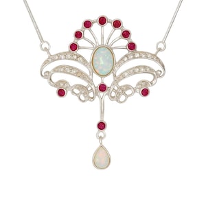 Puede incluir: Collar plateado con un colgante Art Nouveau. El diseño incluye una ópalo ovalado, gemas rojas y cristales transparentes. Un ópalo en forma de lágrima cuelga debajo, sobre fondo blanco.